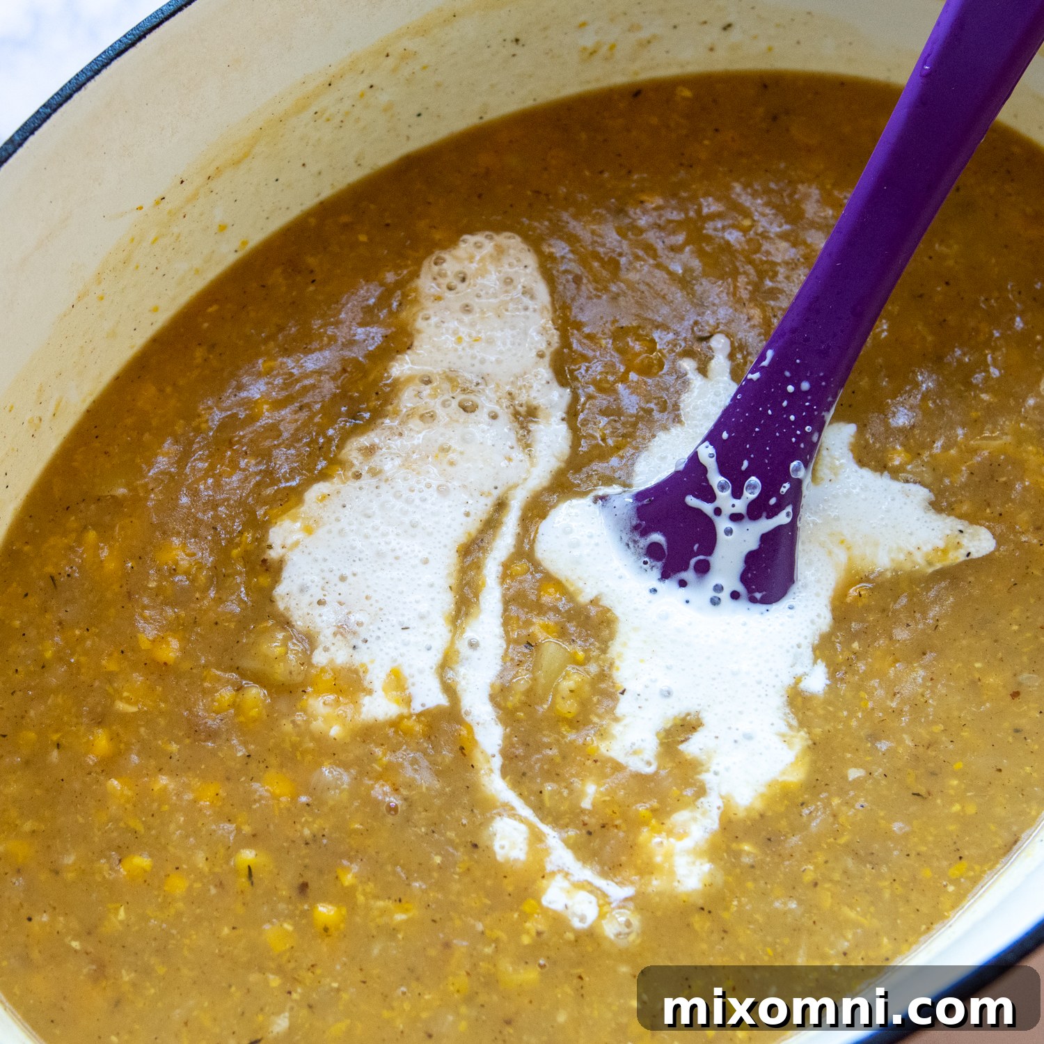 Heavy cream being stirred into the finished corn chowder, creating a rich and smooth consistency, ready for final garnishes and serving.
