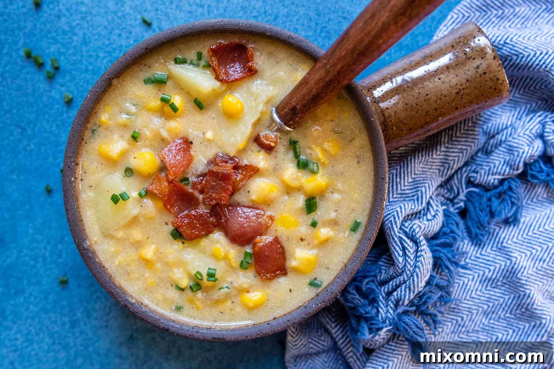 A spoon dipping into a bowl of rich gluten-free corn chowder, served on a vibrant blue background, highlighting its inviting texture.