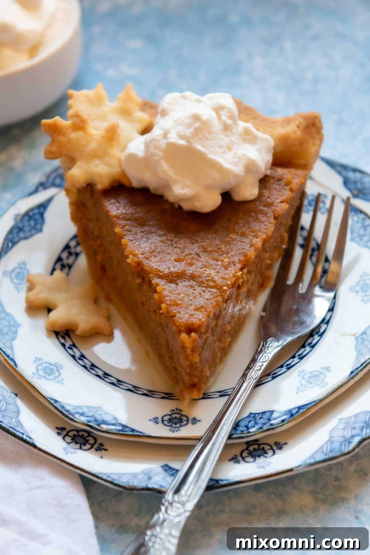 A perfectly baked slice of gluten-free sweet potato pie on a blue and white patterned plate, with a silver fork beside it, inviting a taste of its creamy goodness.