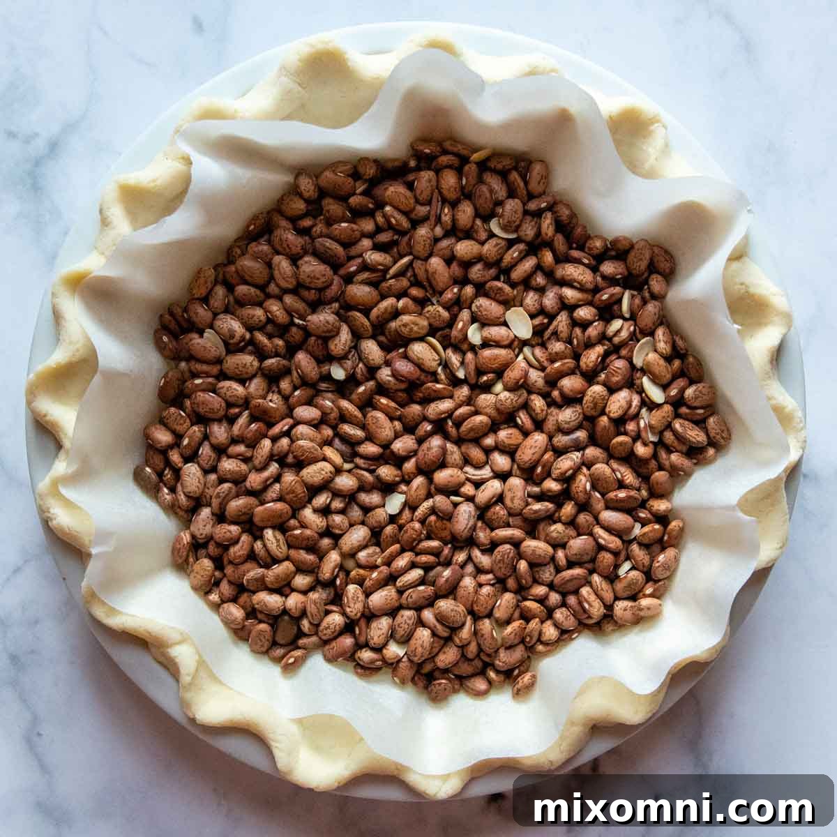 Dried beans neatly arranged as pie weights inside an unbaked pie crust, lined with parchment paper, ready for blind baking.