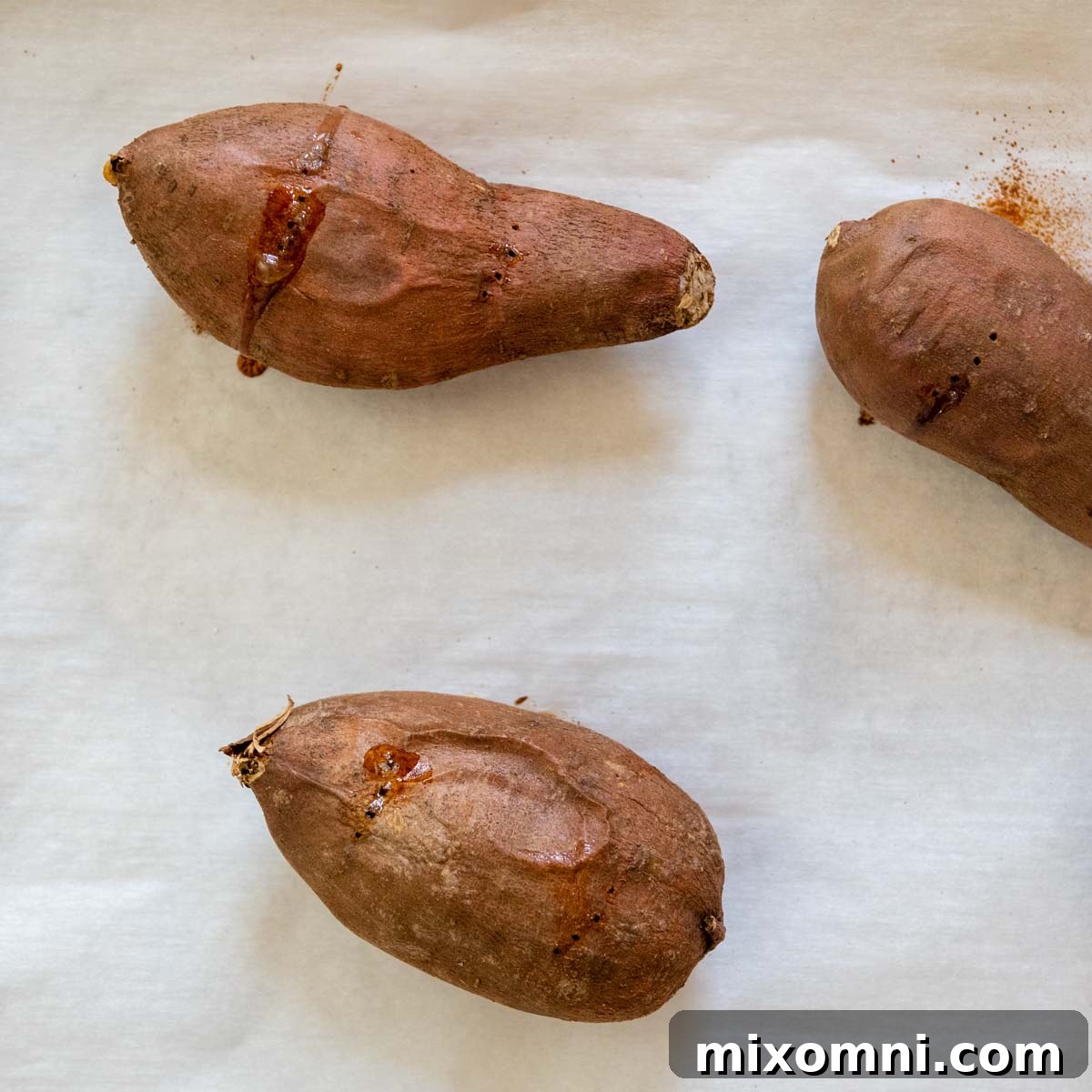 Freshly roasted sweet potatoes, with slightly caramelized skins, arranged on a baking sheet, ready for scooping and pureeing.