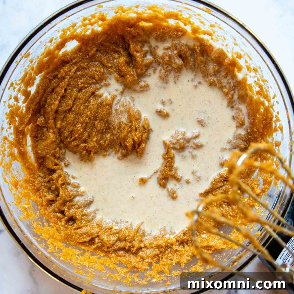 Evaporated milk being poured into the creamy sweet potato pie filling mixture in a large mixing bowl, enhancing its richness and texture.
