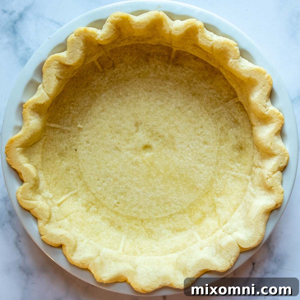 A golden, par-baked gluten-free pie crust in a pie dish, ready to be filled with the creamy sweet potato mixture.