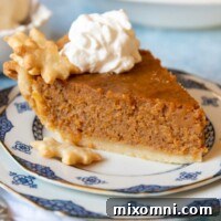 A delicious slice of gluten-free sweet potato pie on a plate with whipped cream, with the full pie blurred in the background.