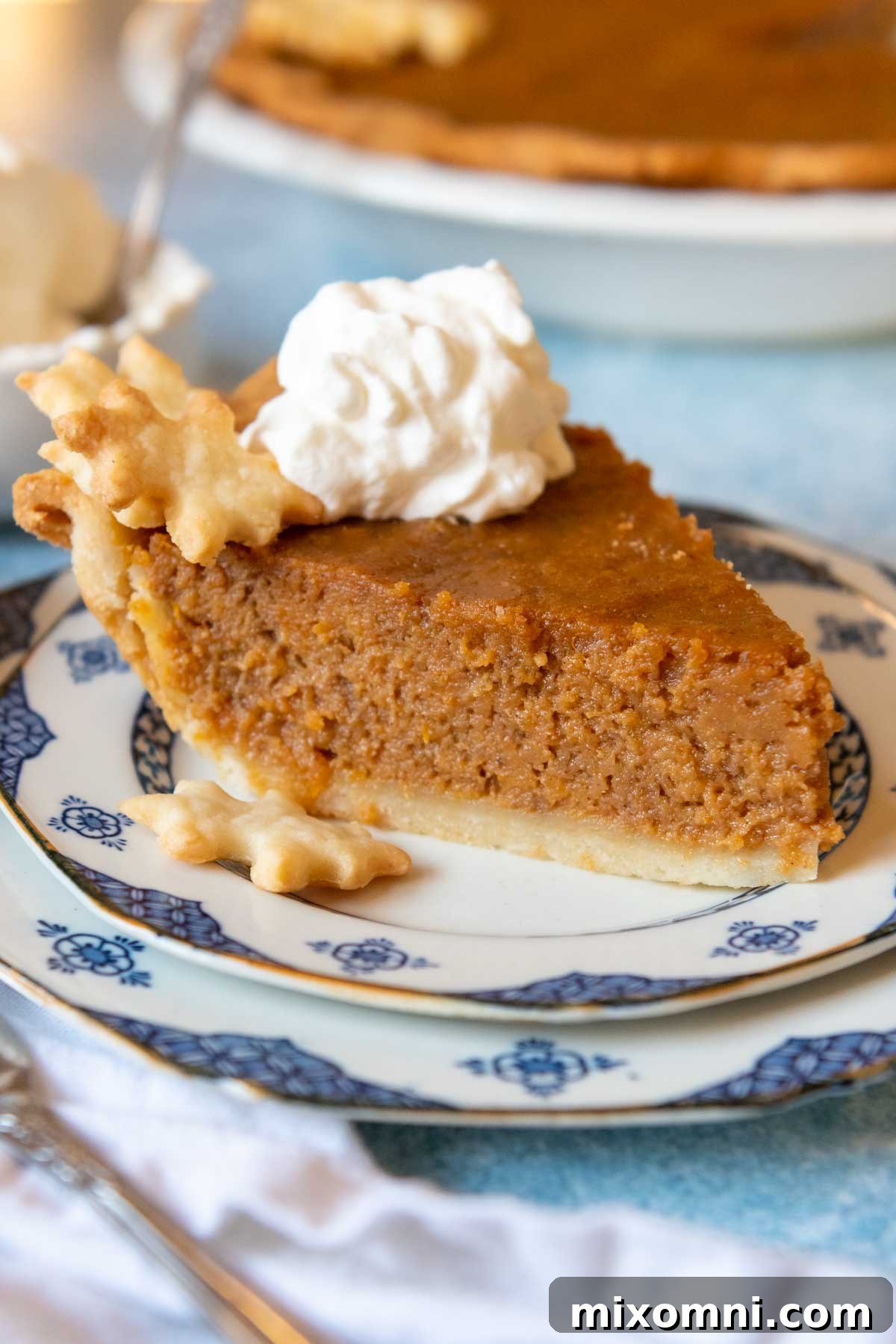 a slice of pie on a plate with whipped cream on top and the whole pie in the background.