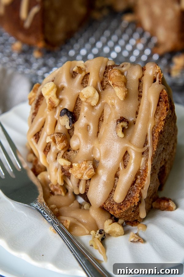 a slice of fresh apple cake on a white plate with brown sugar glaze and walnuts drizzled all over