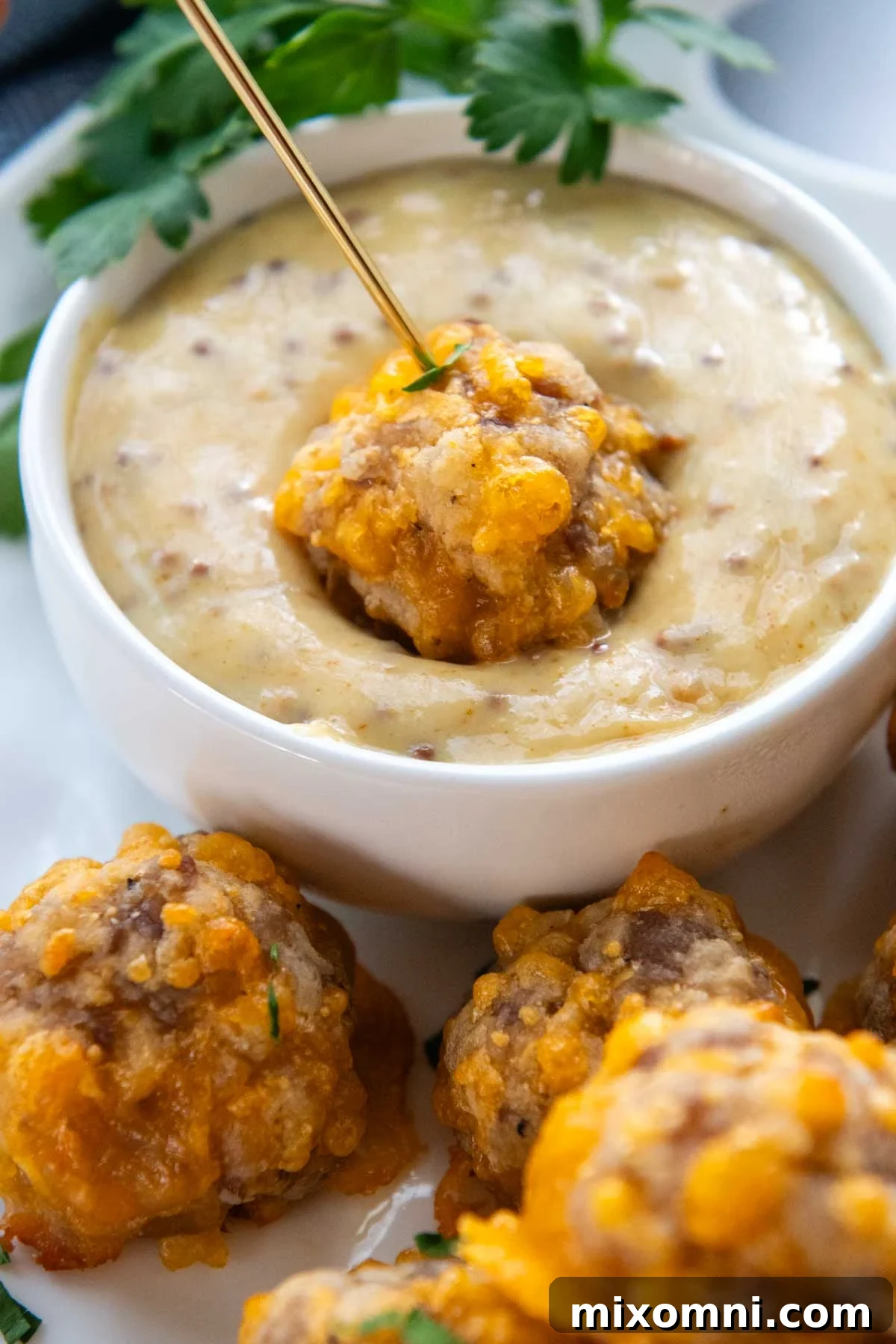 a GF sausage ball being dipped into honey mustard sauce.