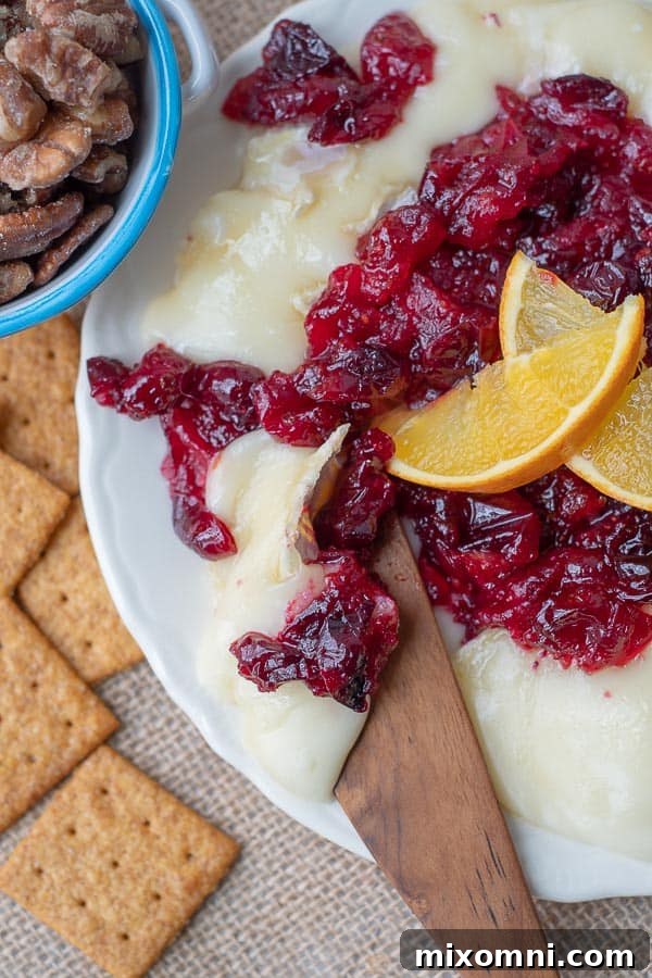 an overhead shot of a wooden knife cutting into cranberry baked brie