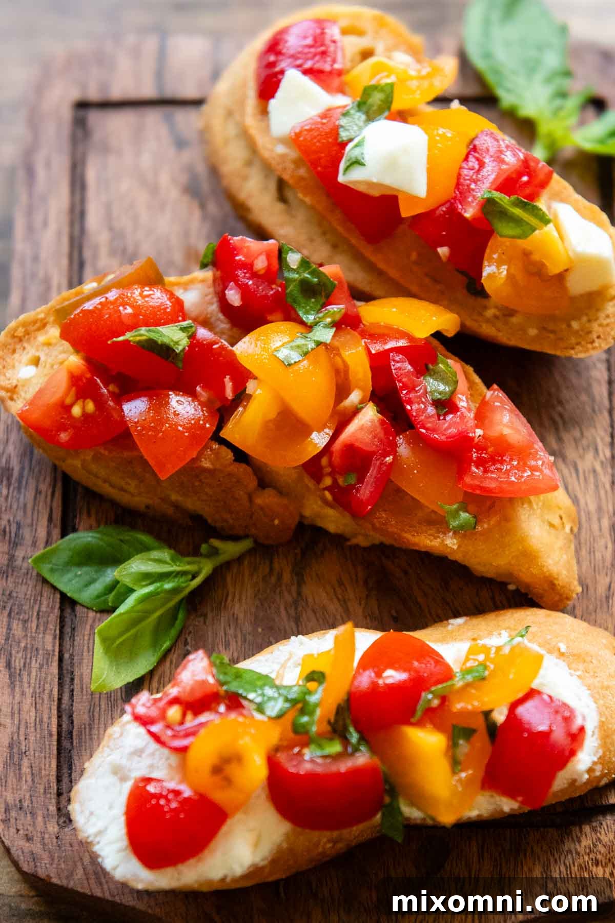 Three bruschetta slices on a wooden cutting board with fresh basil leaves.
