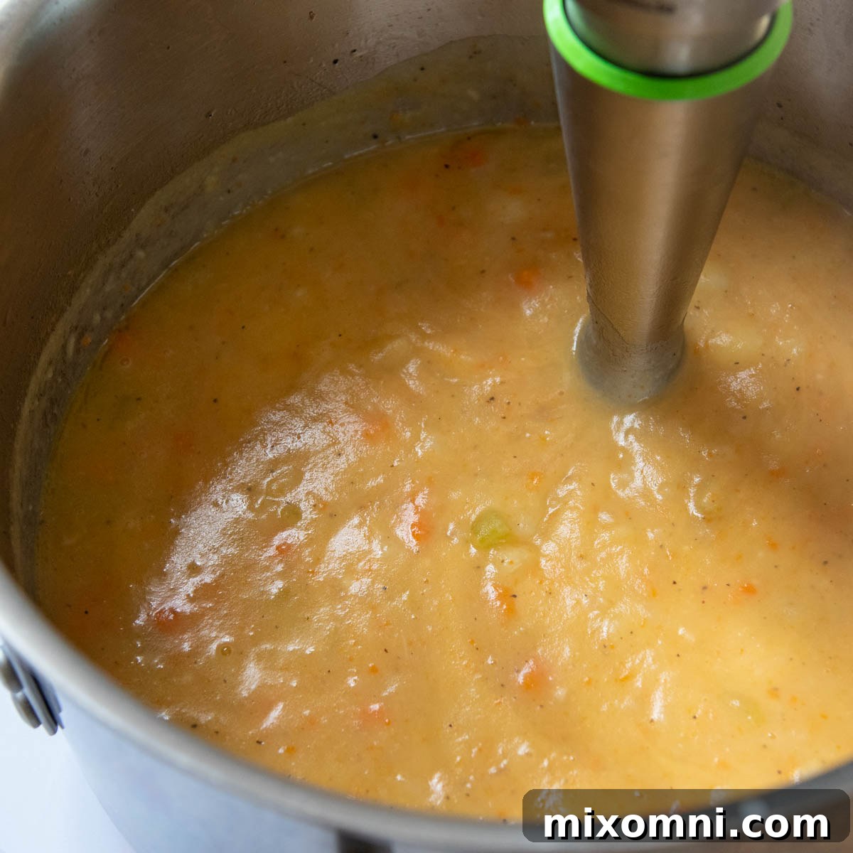 An immersion blender actively pureeing a portion of the potato soup directly in the pot, creating a smooth and creamy texture.