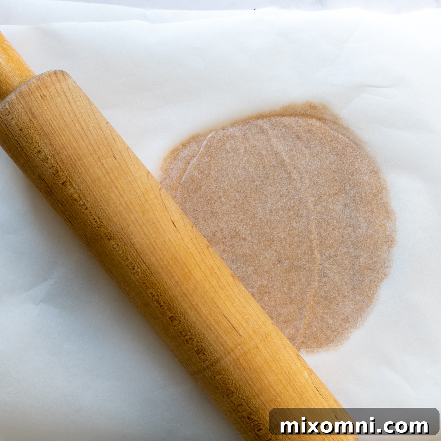 A rolling pin flattening dough between two sheets of parchment paper.