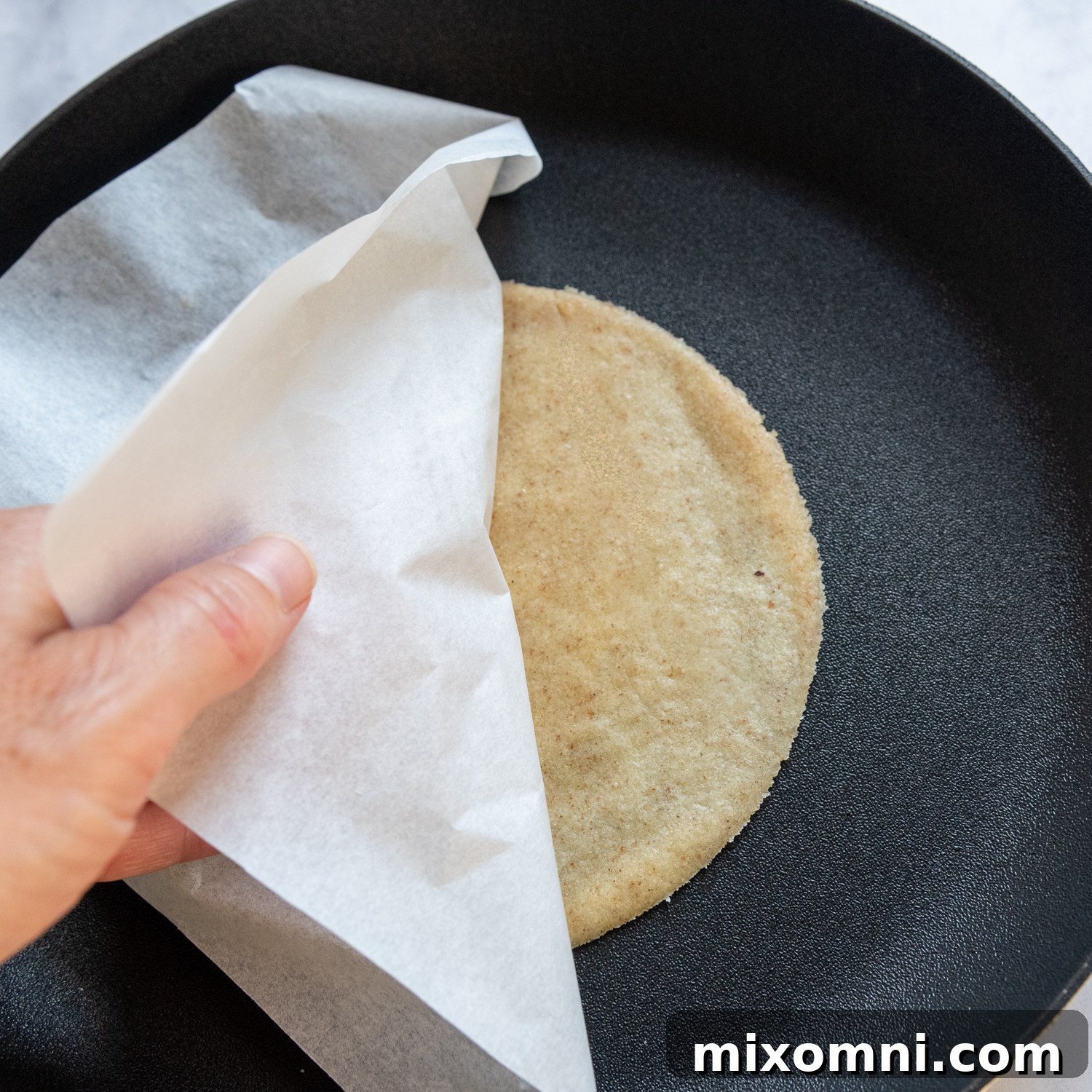 Parchment paper being gently lifted off the tortilla as it cooks in the pan.