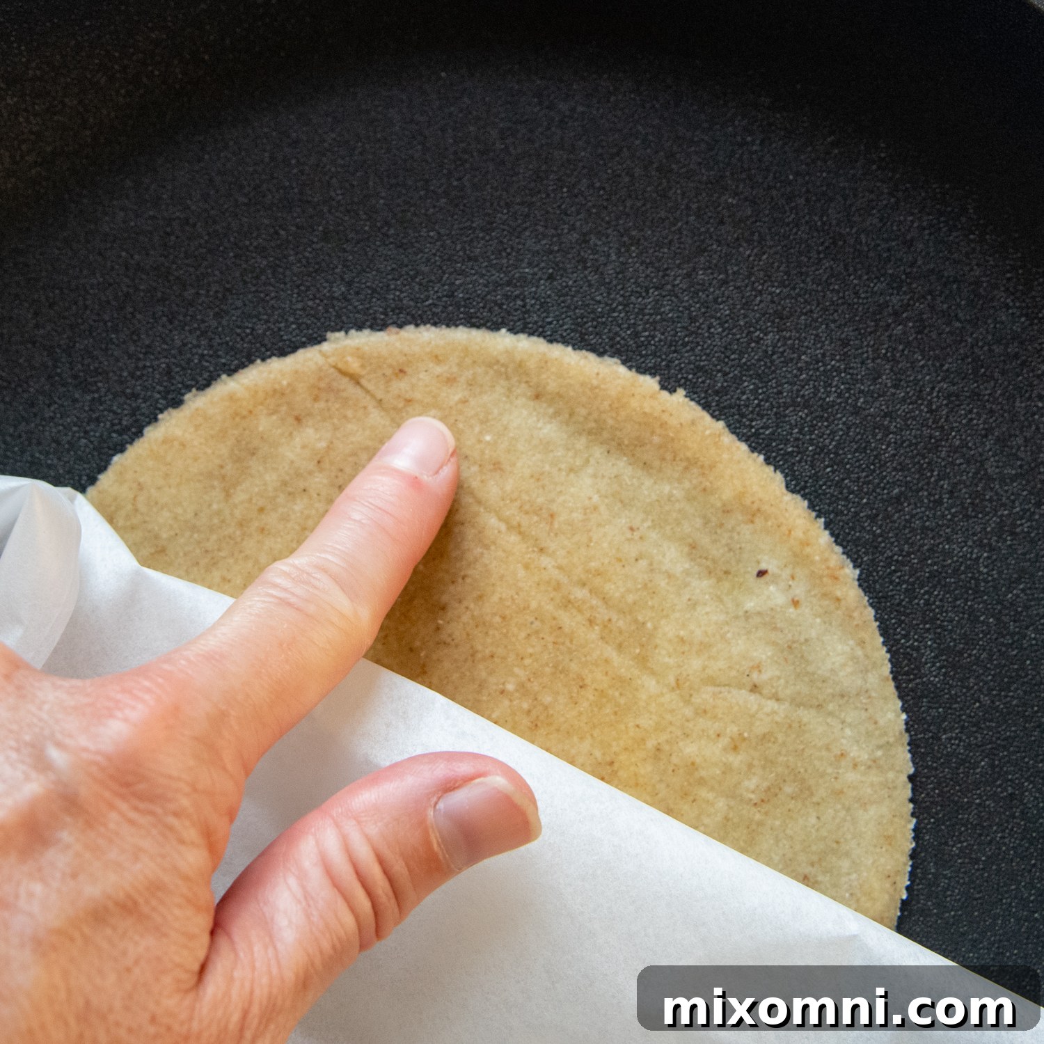 A finger smoothing out creases on the tortilla dough while it cooks.