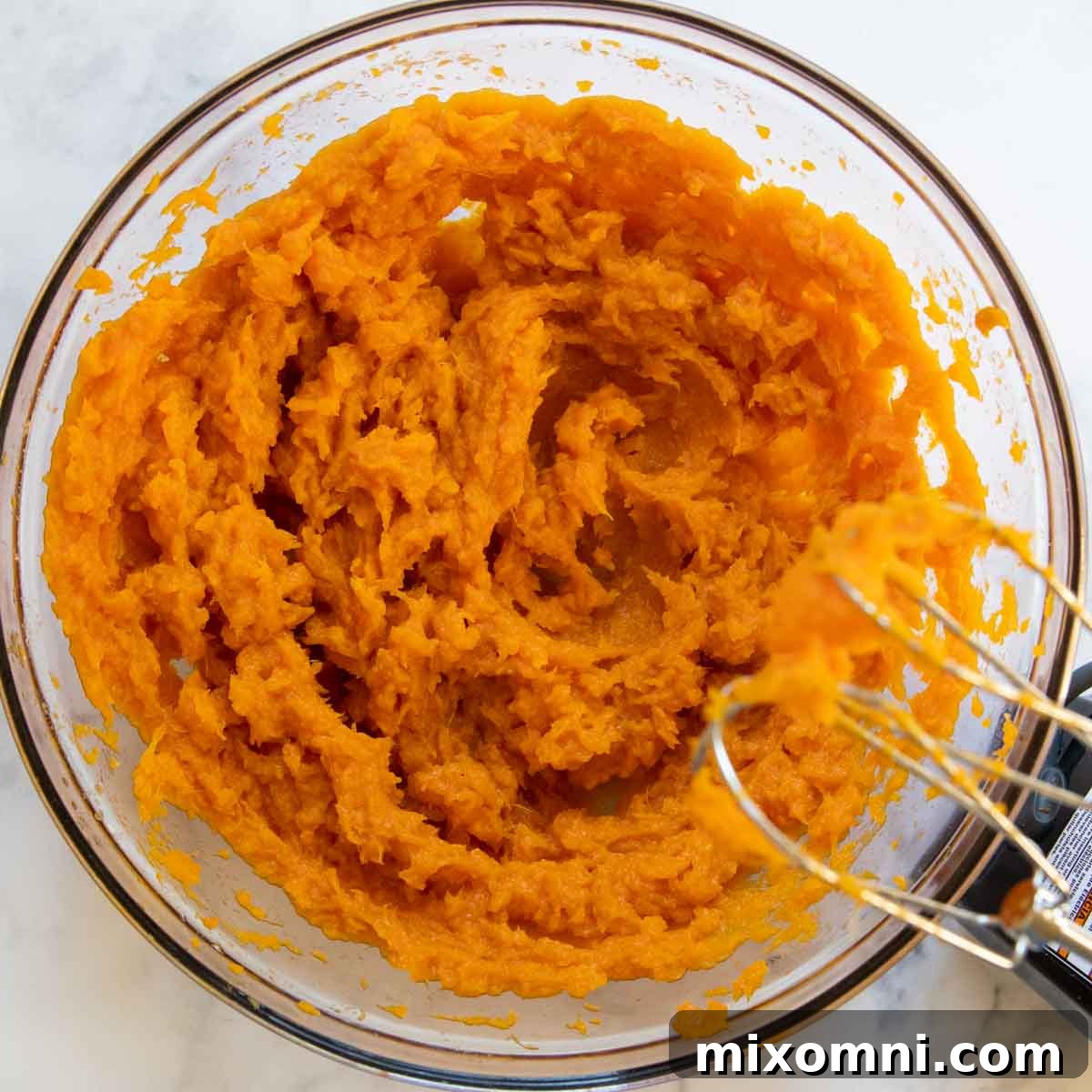 Roasted sweet potatoes being mashed and mixed in a large bowl, ready for the other casserole ingredients.