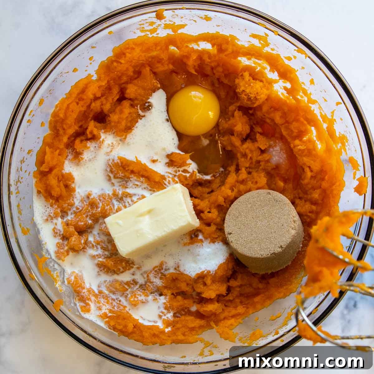 Heavy cream, softened butter, brown sugar, egg, orange zest, and salt added to the mashed sweet potatoes in a bowl.