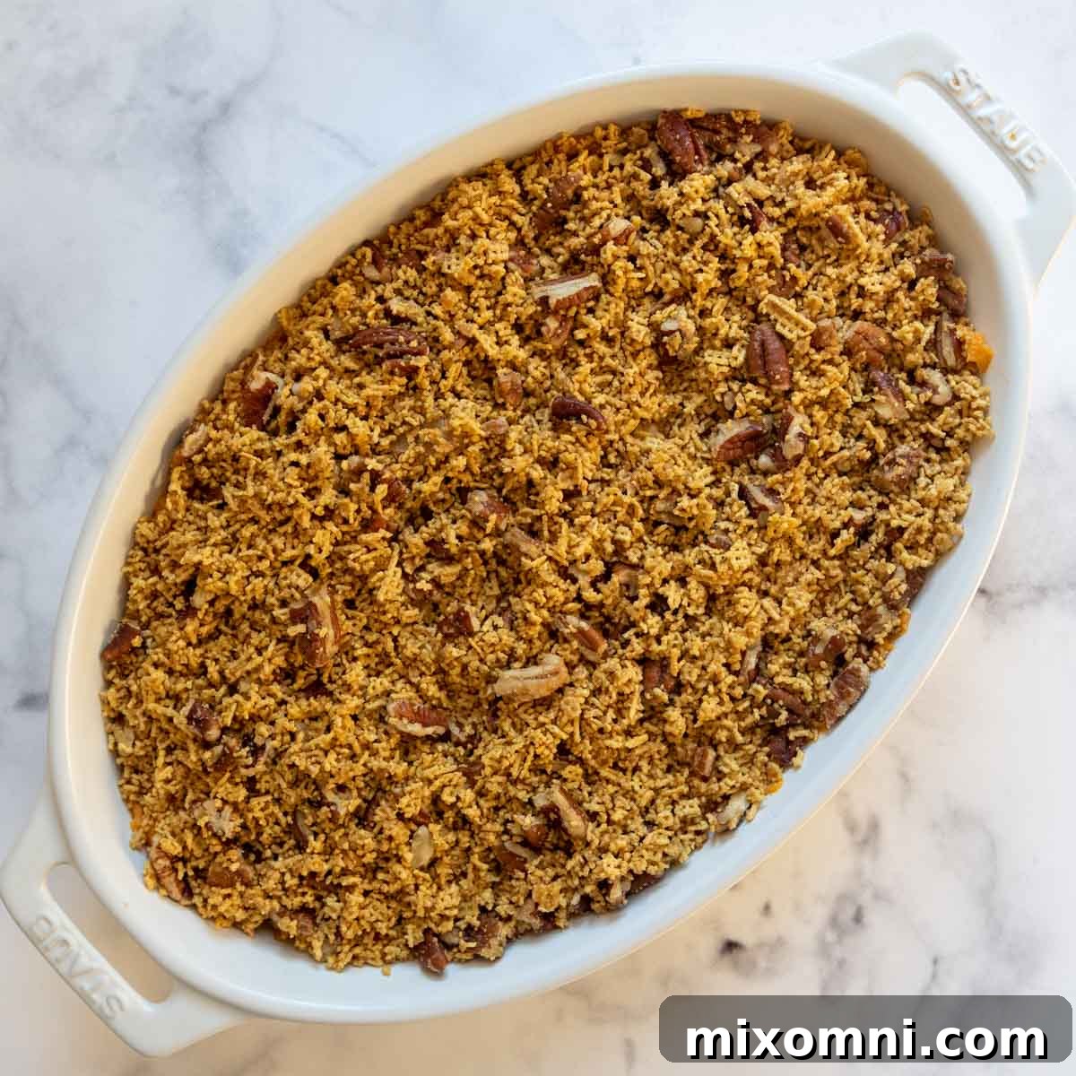 The crunchy pecan Chex cereal topping sprinkled evenly over the sweet potato mixture in a casserole dish, ready for baking.