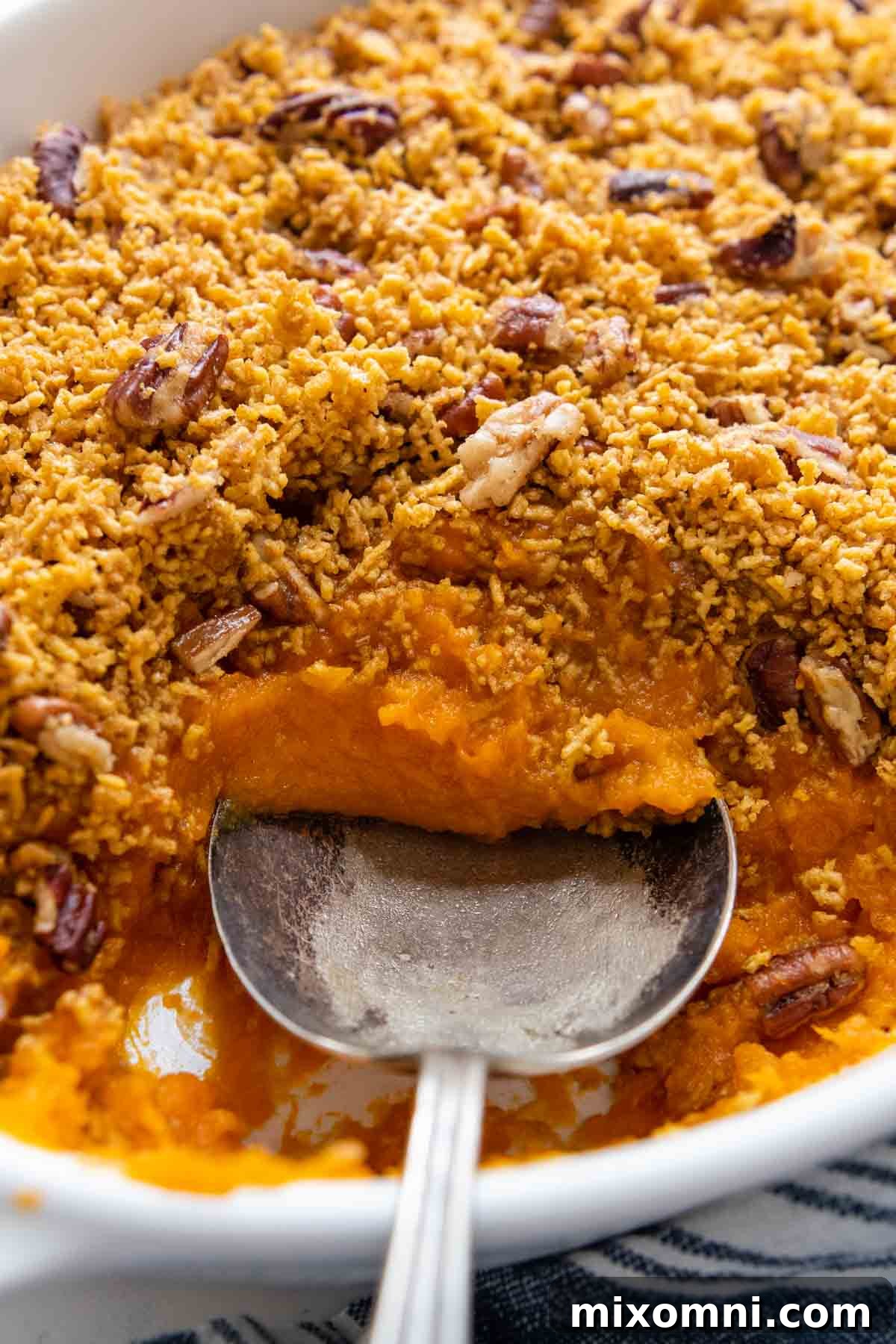 A serving spoon scooping a generous portion of creamy sweet potato casserole from a dish, highlighting its luscious texture and the golden topping.
