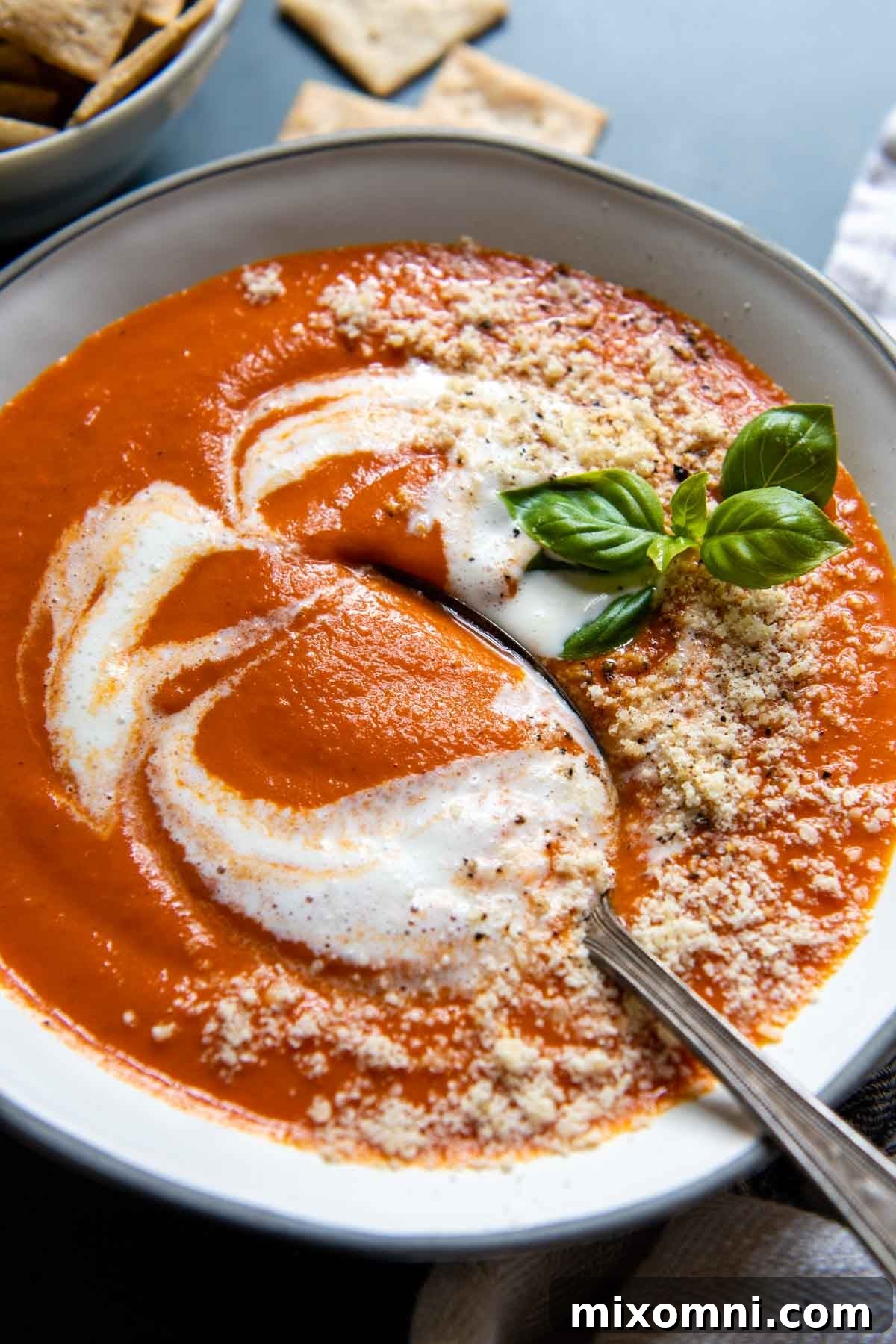 A spoon dipping into a steaming bowl of creamy gluten-free tomato soup, garnished with fresh basil.