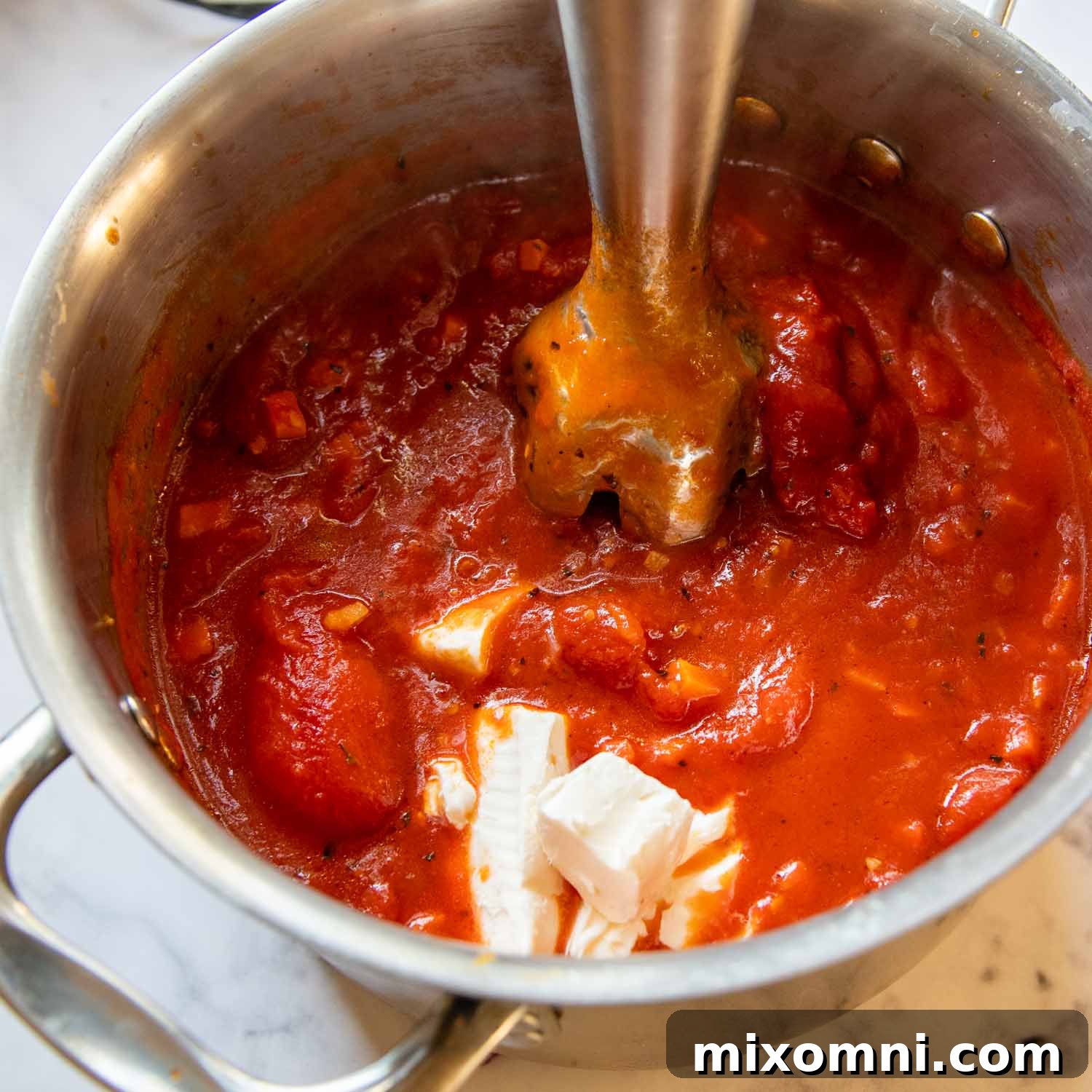 An immersion blender pureeing the soup ingredients, creating a smooth texture.