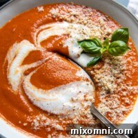 A spoon going into a bowl of tomato soup.