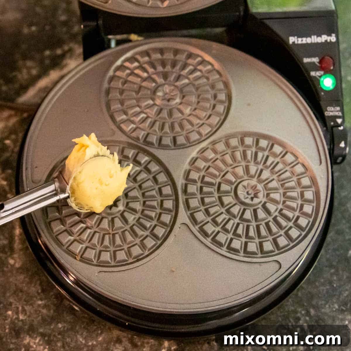 Pizzelle batter being precisely dropped onto a hot pizzelle iron.