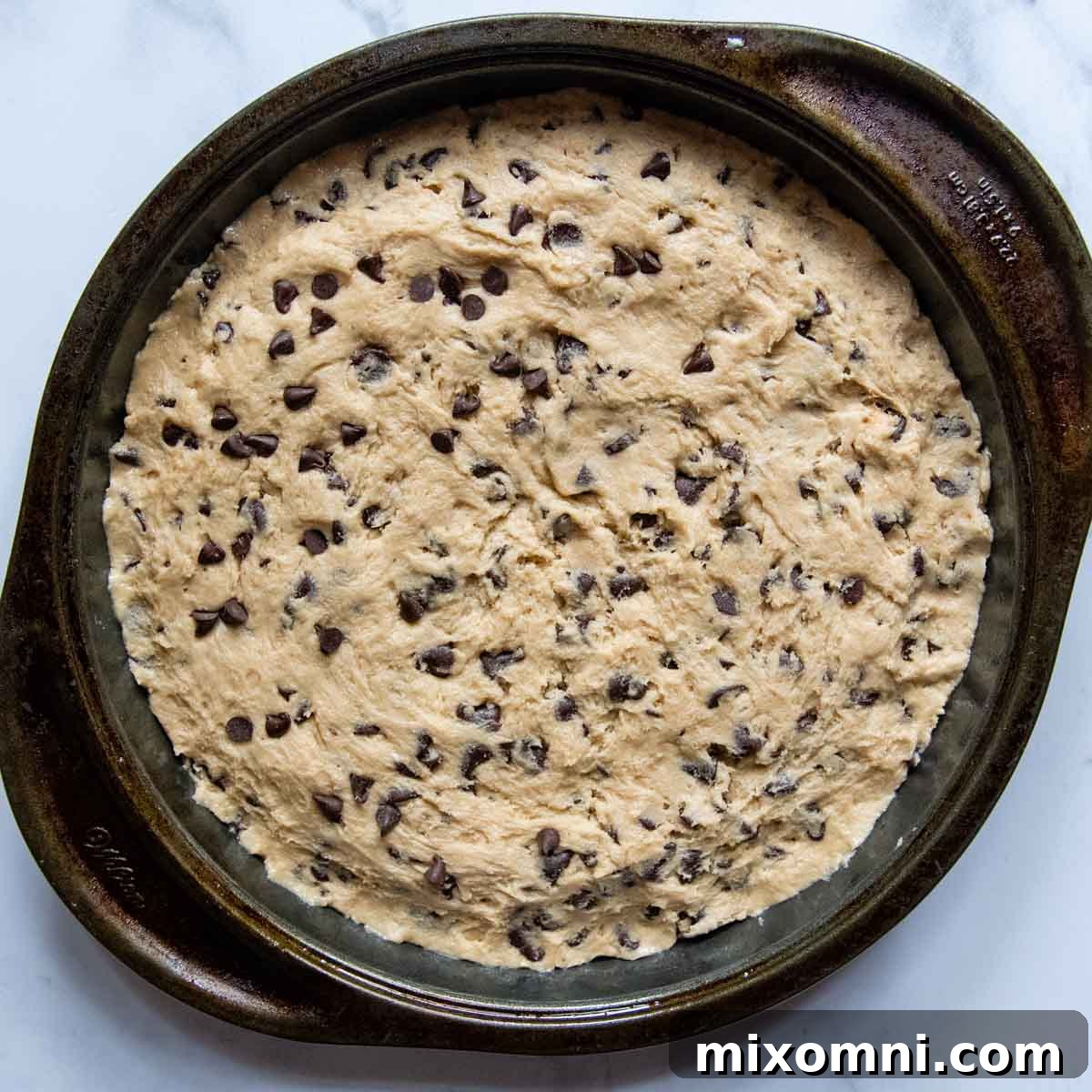 The unbaked gluten-free cookie cake dough perfectly spread in a round baking pan, ready for the oven.
