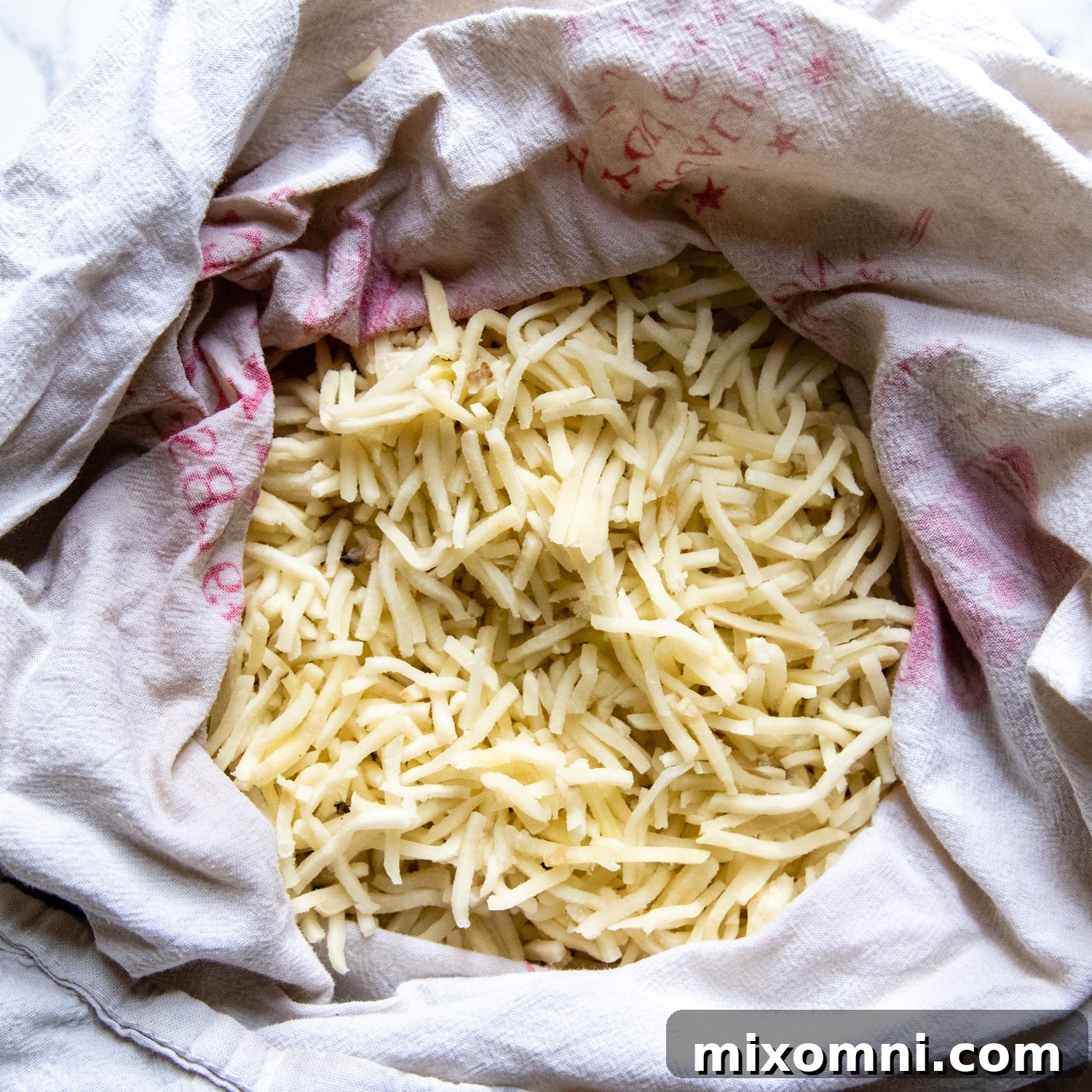 Thawed hash browns being squeezed in a lint-free dish towel to remove excess water.
