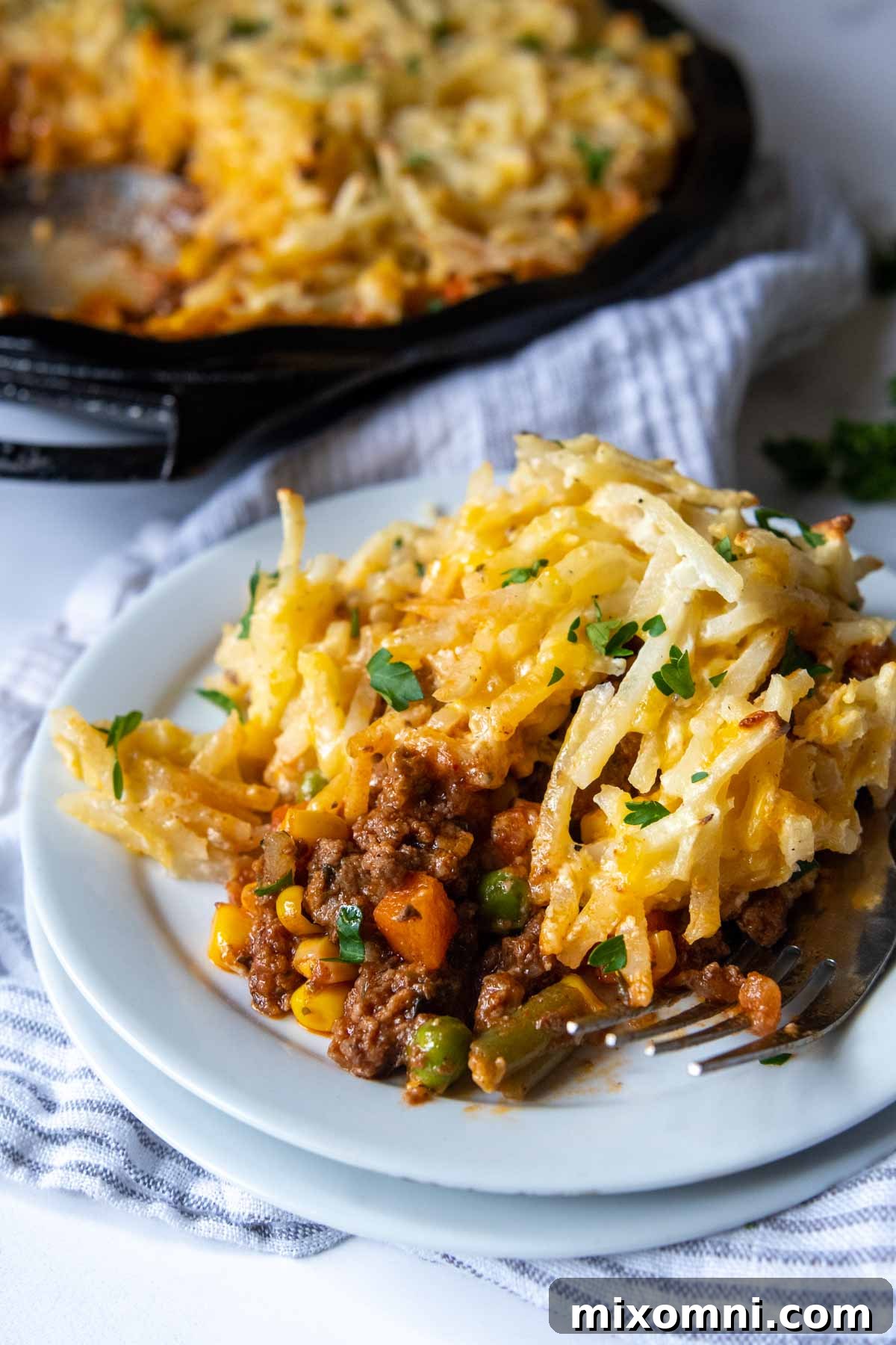 A generous serving of gluten-free cottage pie with a golden hash brown crust on a white plate, ready to be enjoyed.
