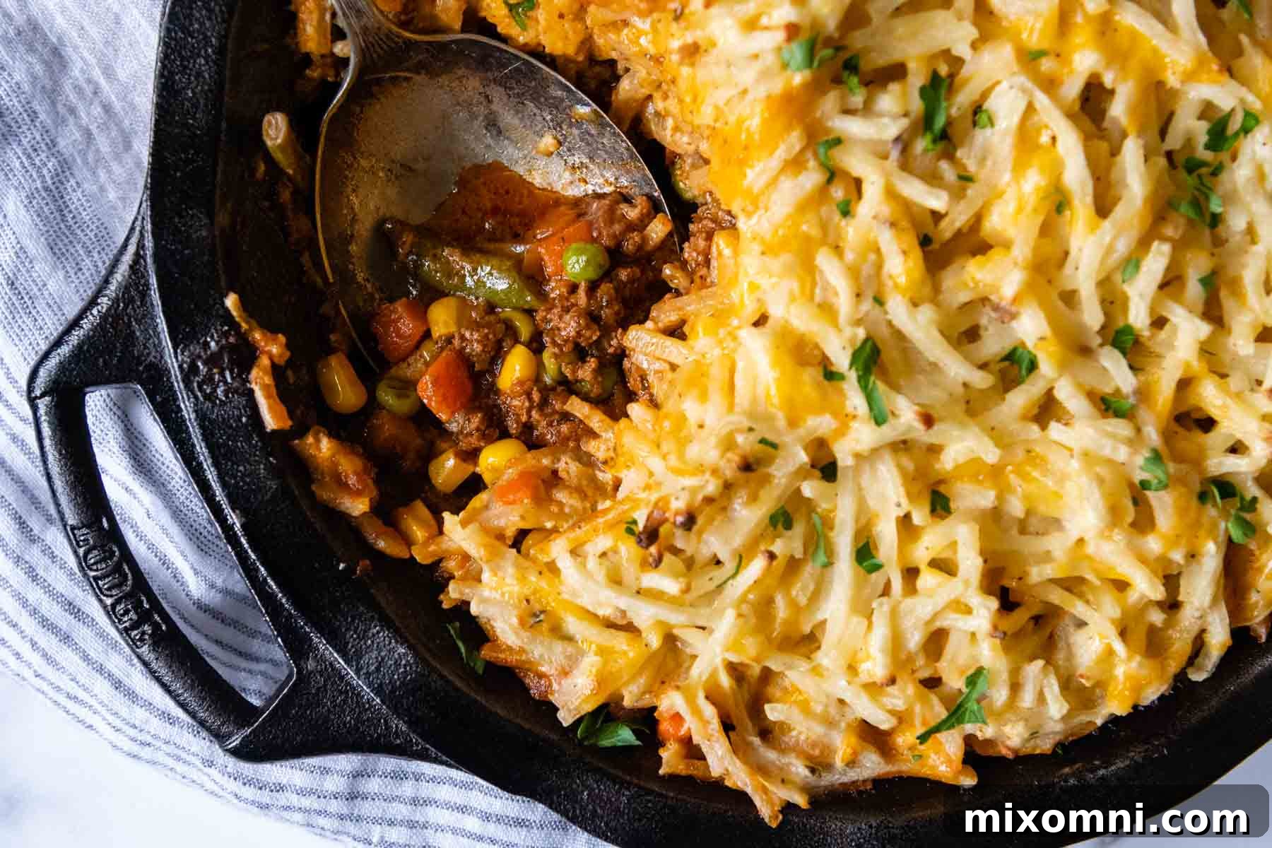 Overhead shot of the cooked shepherd's pie with a serving spoon about to dig in, showcasing the perfect golden topping.
