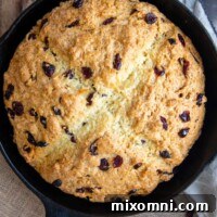 An unsliced loaf of Irish soda bread, baked to a golden finish, sits in a black cast iron skillet, ready to be served.