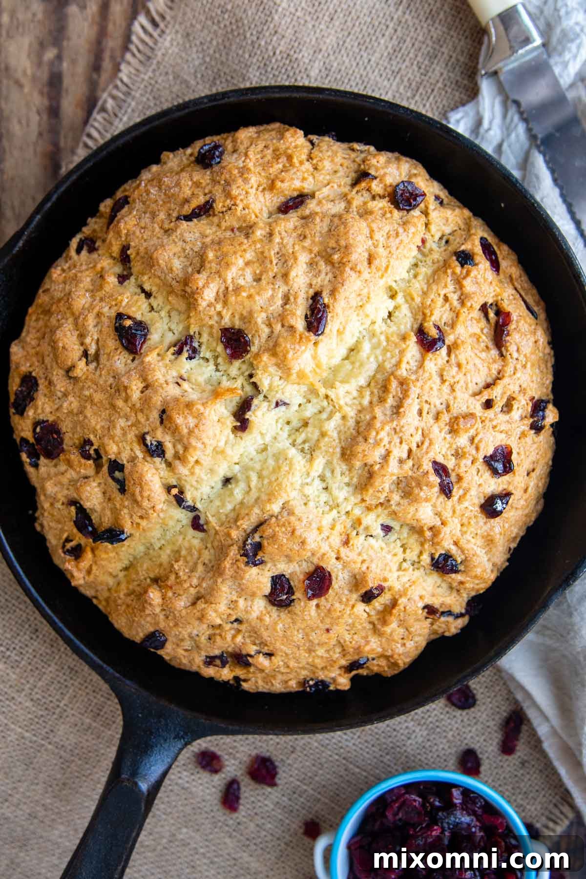 A warm, unsliced loaf of Irish soda bread baked to a perfect golden brown, resting invitingly in a black cast iron skillet.