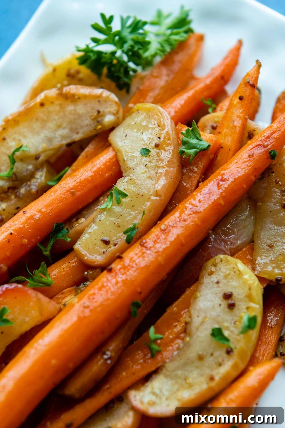 A vibrant side dish of maple Dijon glazed roasted carrots and apples served on a white plate, showcasing their caramelized edges.