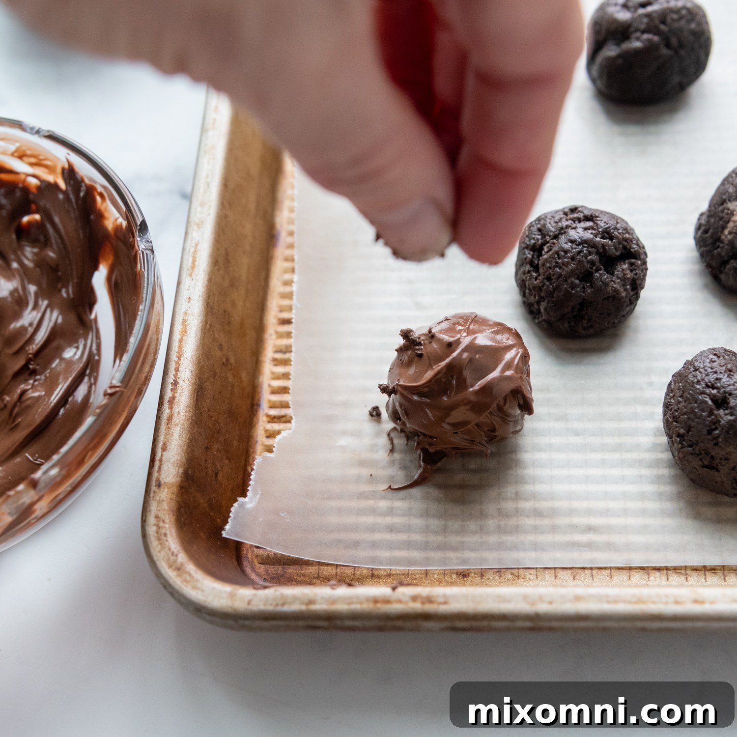 A hand sprinkling crushed Oreo crumbs over a freshly dipped gluten-free Oreo truffle, adding a decorative and textural finish.