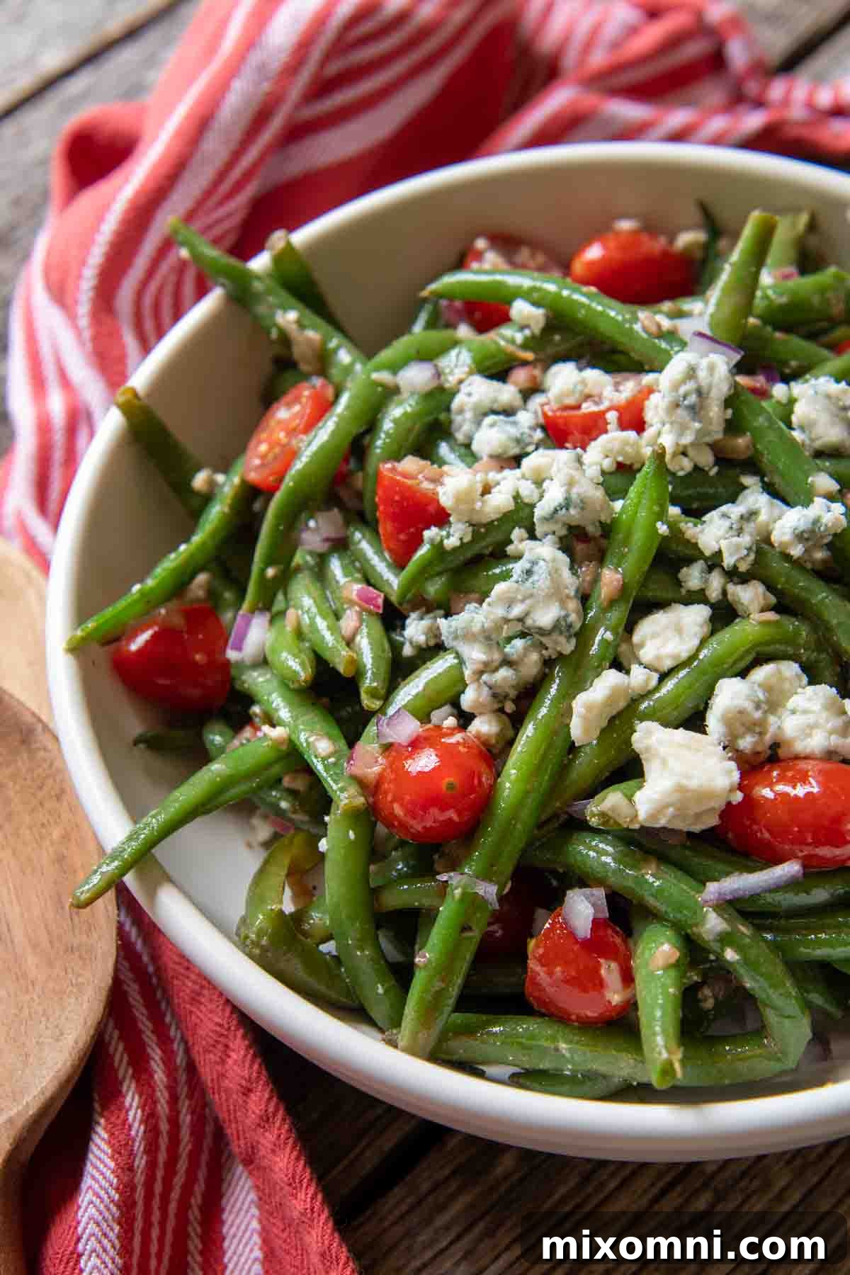 A close-up of a vibrant serving bowl filled with marinated green bean salad, featuring blue cheese and tomatoes.