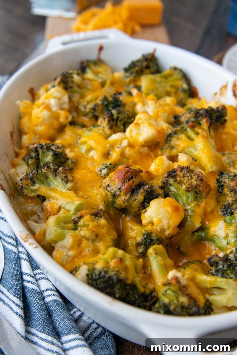 A close-up view of a baked broccoli and cauliflower casserole, topped with bubbling, melted cheddar cheese.