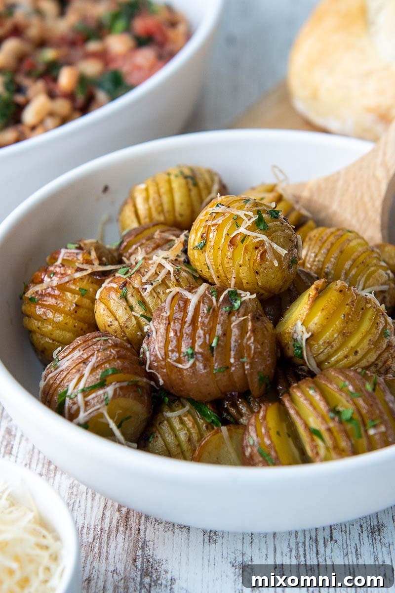 A wooden spoon serving a scoop of golden mini hasselback potatoes from a rustic serving bowl.