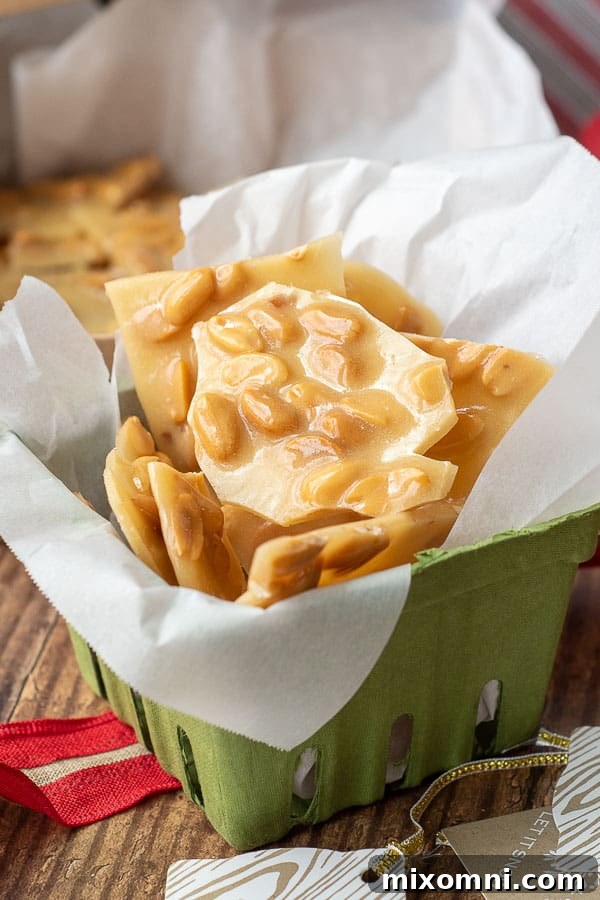 peanut brittle in a green gift box with red ribbon laying next to it