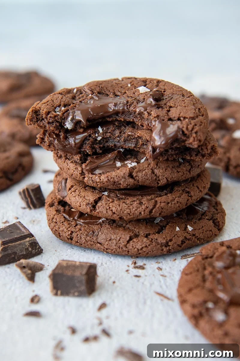 a stack of cookies with the top two having bites taking out and chocolate chunks laying around it