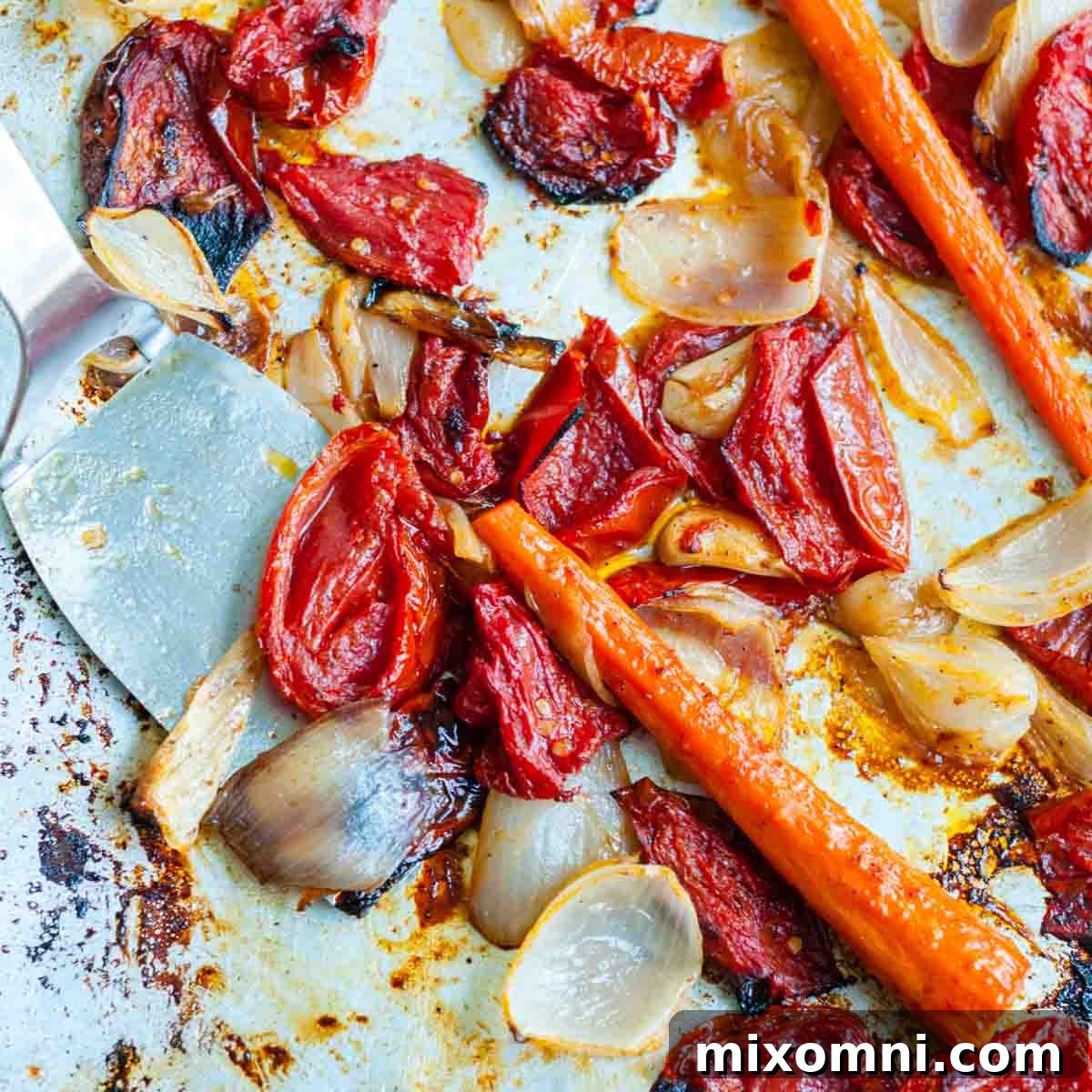 Roasted plum tomatoes, carrots, garlic, and onions on a sheet pan, showing caramelization.