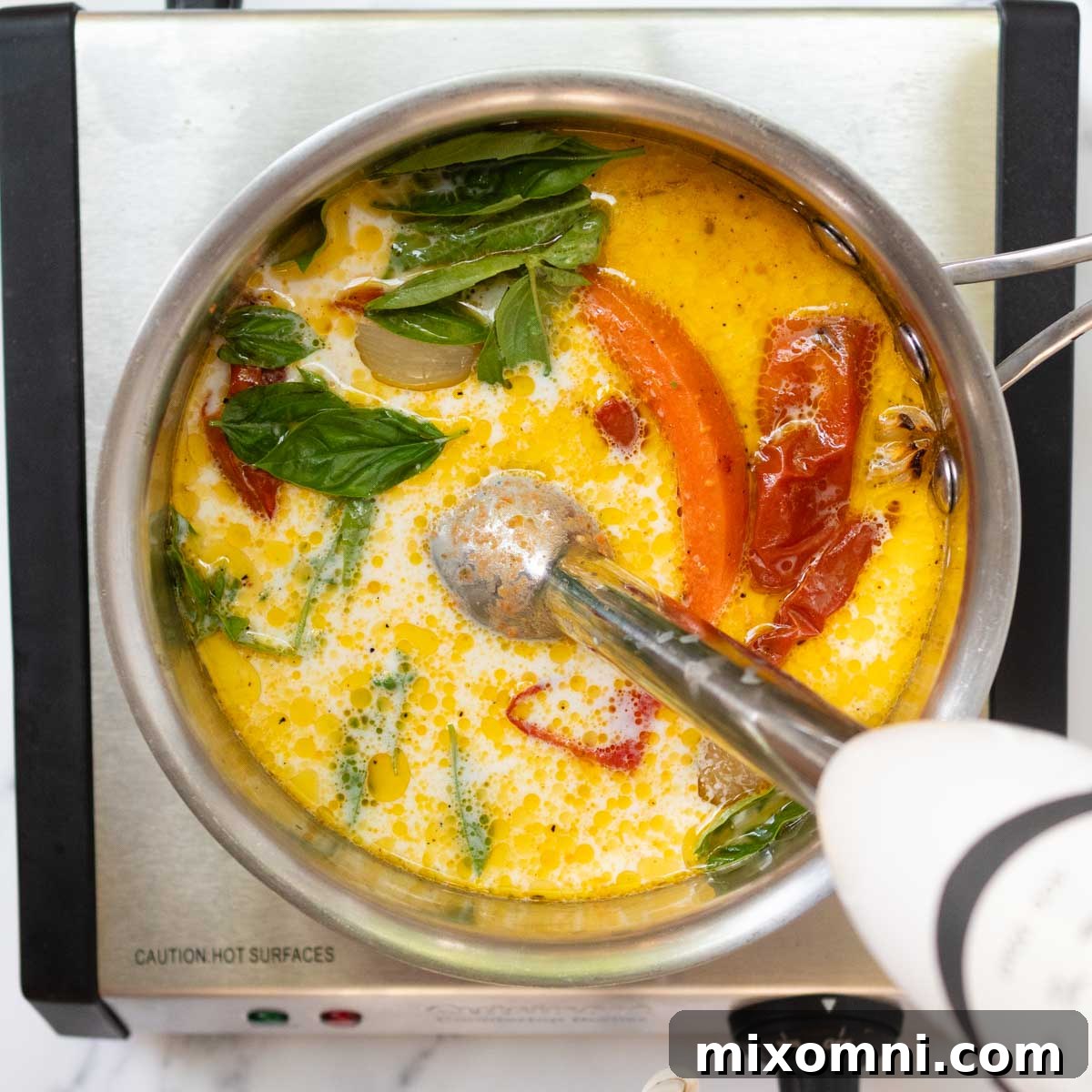 An immersion blender processing the tomato soup ingredients directly in a pot.