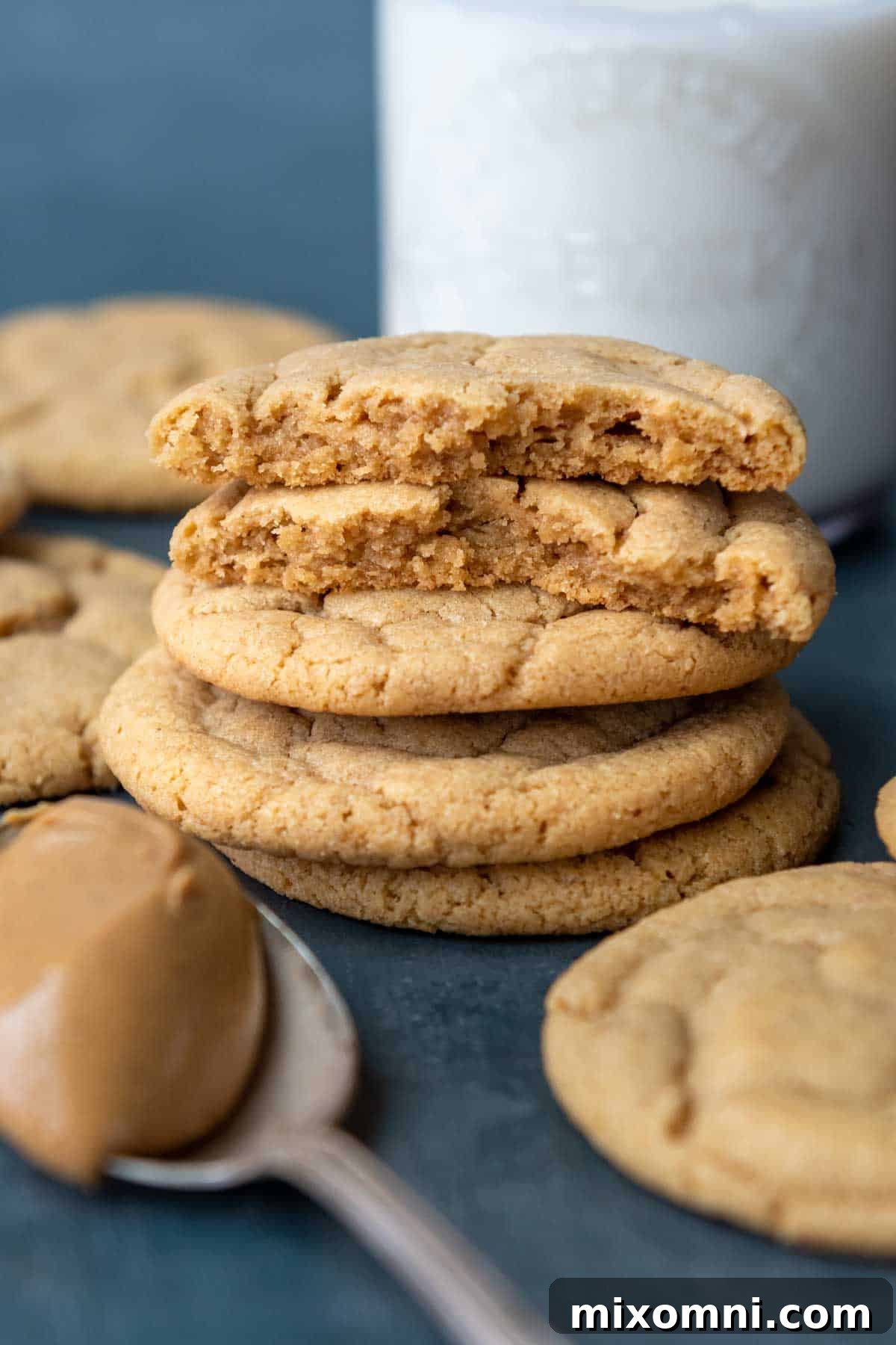 Two broken gluten-free peanut butter cookies reveal their soft, gooey centers, with a glass of milk in the background.