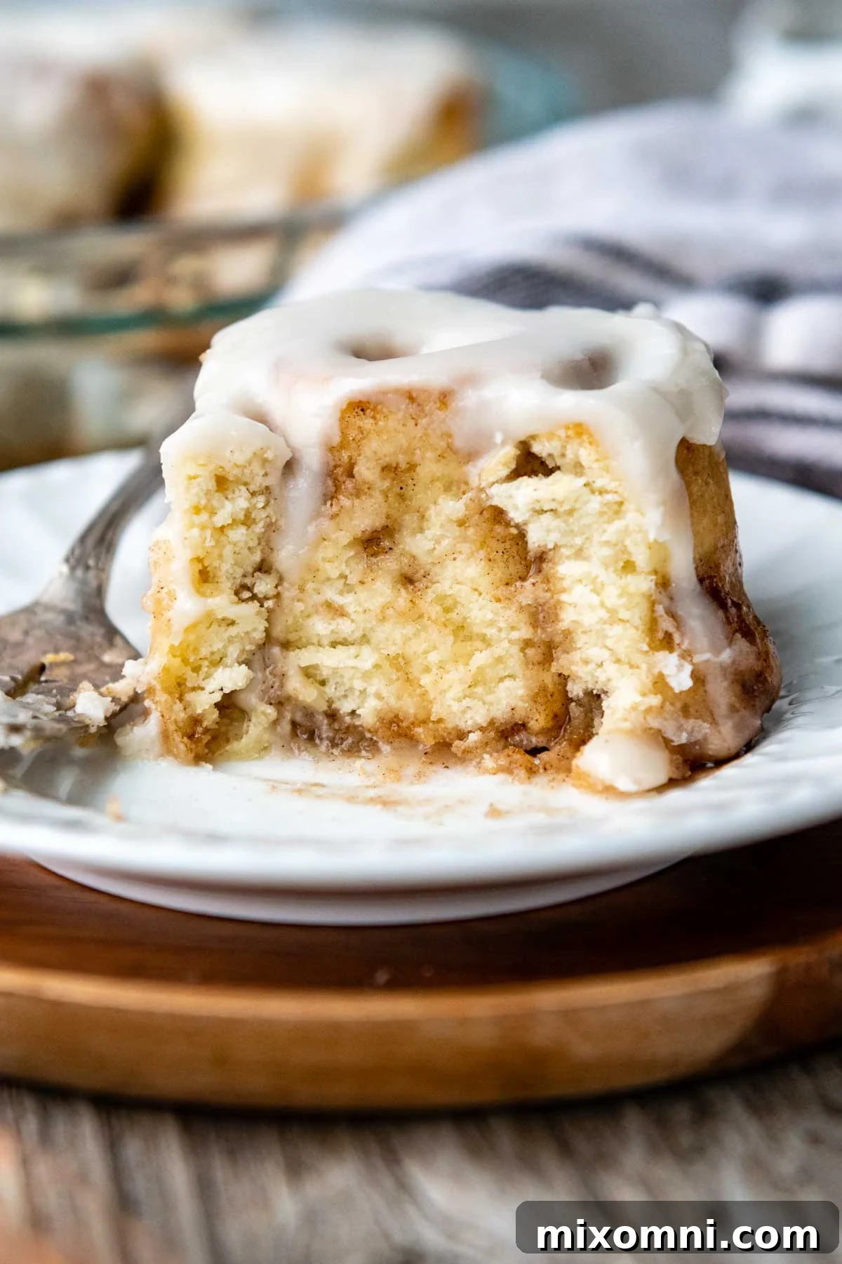 a cinnamon bun with a bite taken out on a white plate.