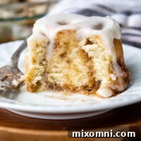 a cinnamon bun with a bite taken out on a white plate.