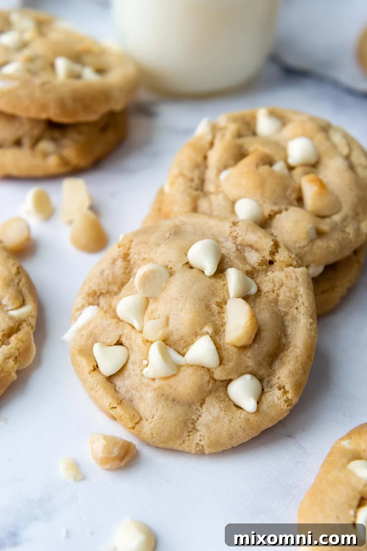 Freshly baked gluten-free white chocolate macadamia nut cookies cooling on a white marble surface, surrounded by loose macadamia nuts and white chocolate chips, inviting you to indulge in their deliciousness.