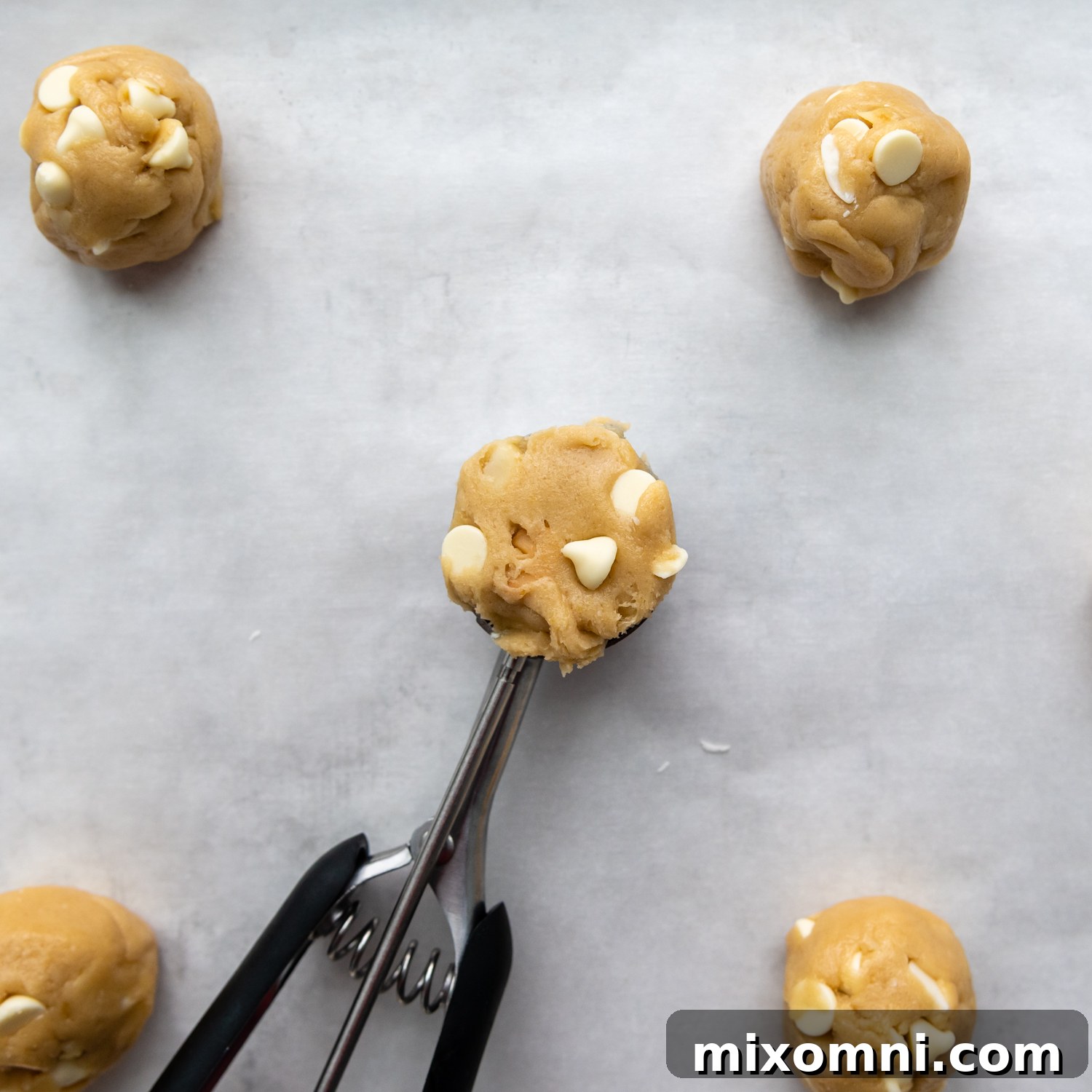 Portioned cookie dough balls, neatly scooped onto a parchment-lined baking sheet, ready for the oven.