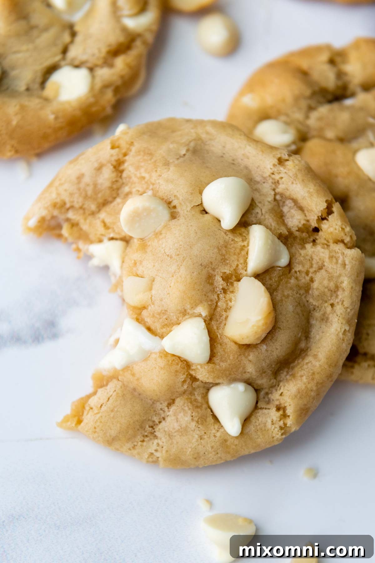 A close-up top view of a perfectly baked gluten-free white chocolate macadamia nut cookie with a bite taken out, revealing its soft, chewy interior filled with chips and nuts.