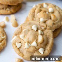 Gluten-free white chocolate macadamia nut cookies arranged on a white marble surface with loose nuts and chocolate chips.