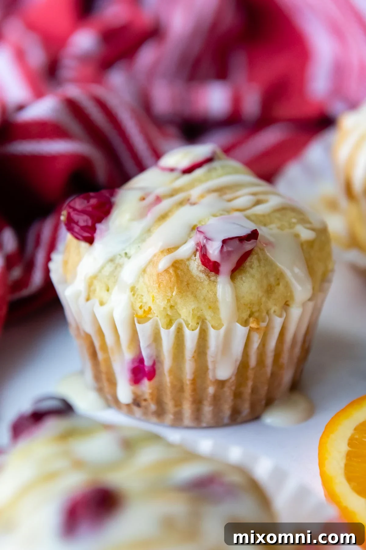 A whole gluten-free cranberry orange muffin, perfectly glazed, rests on a pristine white marble surface, ready to be enjoyed.