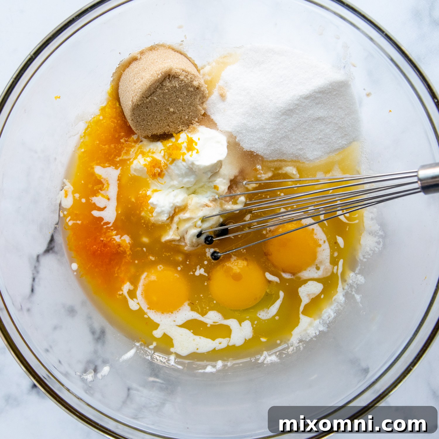 Wet ingredients being whisked together in a large glass bowl, creating a smooth, golden mixture for the muffin batter.