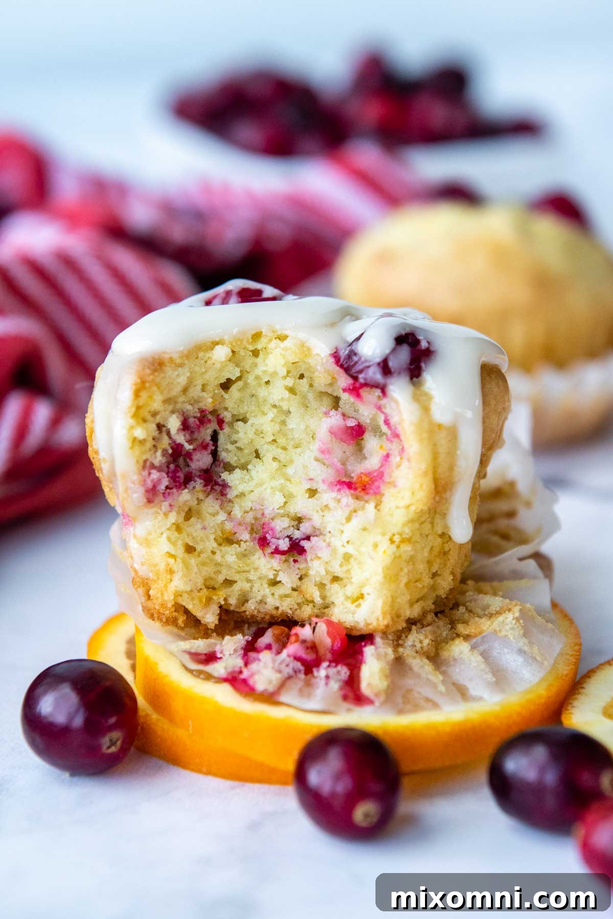 A freshly baked gluten-free cranberry orange muffin, perfectly glazed, with a bite taken out to reveal its soft, moist interior.
